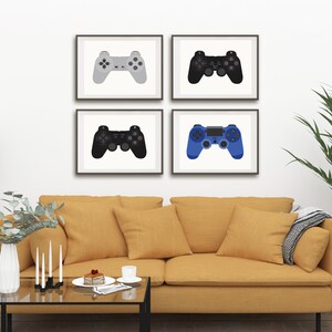 May include: Four framed prints of different colored video game controllers. The controllers are gray, black, blue, and white. The prints are hanging on a white wall above a yellow couch.