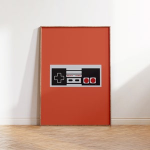 May include: A framed print of a retro video game controller on a bright orange background. The controller is black and white with red buttons and the words "SELECT" and "START" printed on it.