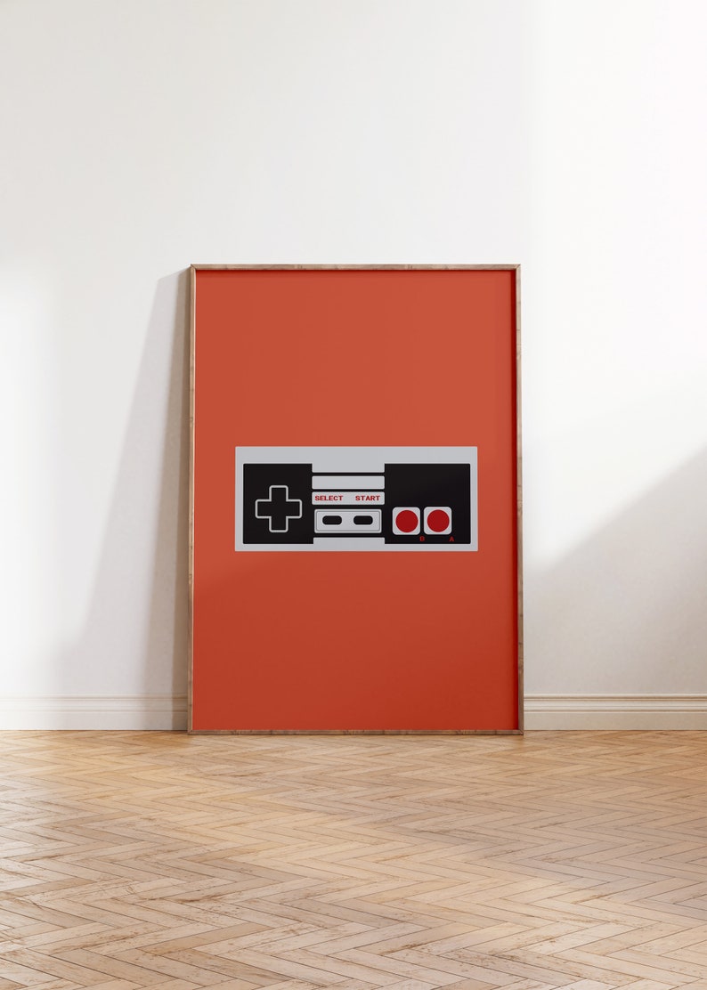 May include: A framed print of a retro video game controller on a bright orange background. The controller is black and white with red buttons and the words "SELECT" and "START" printed on it.