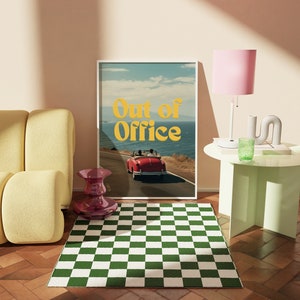 May include: A framed print with a retro aesthetic featuring a red car driving on a winding road with the text "Out of Office" in yellow letters. The print is hanging on a wall above a green and white checkered rug.