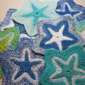 May include: A collection of handmade crochet starfish in various shades of blue, green, and white. Each starfish has a central hole and a contrasting color starfish design. The items are likely kitchen or home decor.