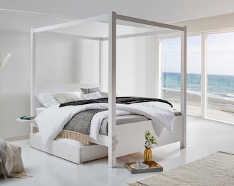 May include: A white four-poster canopy bed frame with a solid headboard and footboard. The bed is dressed with white linens, a gray textured throw blanket with fringe, and a black throw blanket. A white storage drawer is visible underneath the bed.