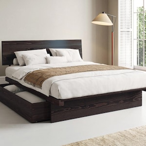 May include: A dark brown wooden platform bed frame with a rectangular headboard and a low-profile base. The bed features a pull-out storage drawer on the side, topped with a white mattress, white pillows, and a brown textured throw blanket.