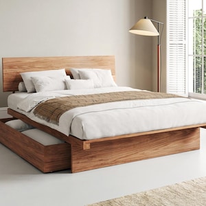 May include: A platform bed frame crafted from light brown wood with a prominent headboard and a built-in storage drawer at the base. The bed is dressed with white linens, two white pillows, a small bolster pillow, and a brown textured runner.