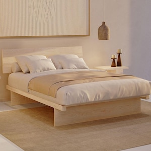 May include: A light-coloured wooden platform bed frame with a horizontal slat headboard. The bed is dressed with white pillows and a beige throw blanket. The frame features a low-profile design with solid wood panel supports at the base.