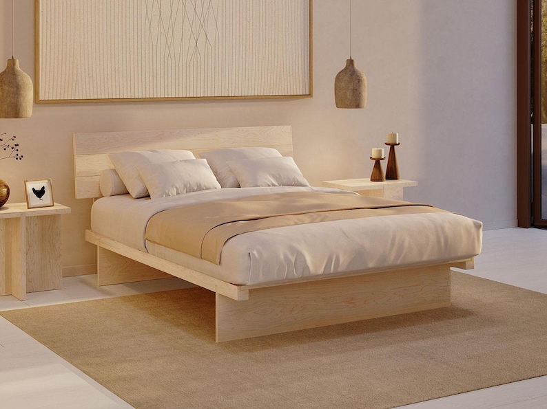 May include: A light-coloured wooden platform bed frame with a horizontal slat headboard. The bed is dressed with white pillows and a beige throw blanket. The frame features a low-profile design with solid wood panel supports at the base.