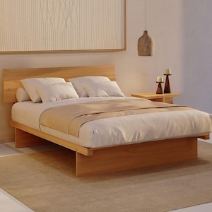 May include: A low-profile platform bed frame crafted from light-toned wood, featuring a horizontal slatted headboard. The bed is dressed with white pillows, a white duvet, and a tan runner, flanked by two matching wooden nightstands with candles.
