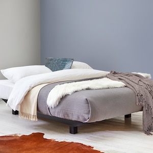 May include: A gray platform bed with a white duvet, a beige throw blanket, and a white faux fur throw. The bed is on a white wood floor with a brown cowhide rug.