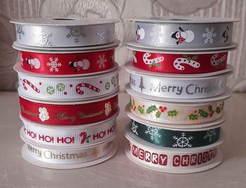 May include: A stack of Christmas-themed ribbon spools. Designs include snowflakes, snowmen, candy canes, and holly. Colors include red, white, green, and silver. Some ribbons have the text "Merry Christmas" and "HO! HO! HO!".
