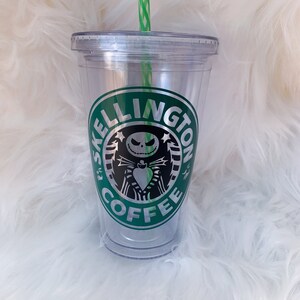 May include: Clear plastic tumbler with a green and white striped straw. The tumbler features a green and silver logo with the words "SKELLINGTON COFFEE" and a graphic of Jack Skellington from The Nightmare Before Christmas.