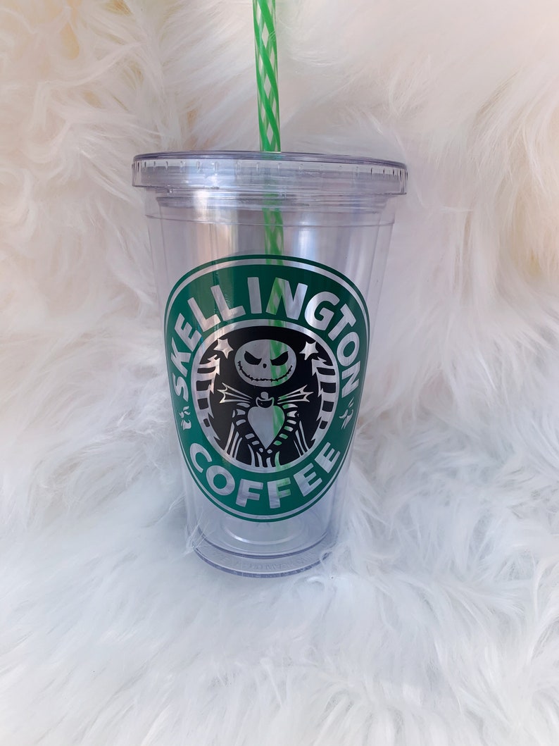 May include: Clear plastic tumbler with a green and white striped straw. The tumbler features a green and silver logo with the words "SKELLINGTON COFFEE" and a graphic of Jack Skellington from The Nightmare Before Christmas.