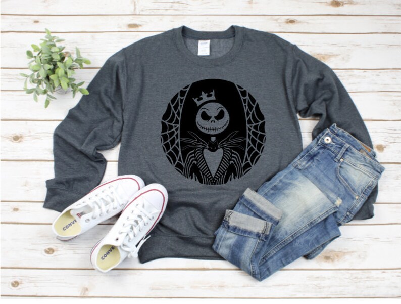 Pu&ograve; includere: Felpa grigio scuro con grafica nera di Jack Skellington da Nightmare Before Christmas, all'interno di un cerchio con un disegno a ragnatela. Sono presenti anche scarpe da ginnastica bianche e jeans blu.