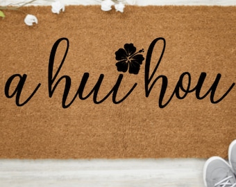 May include: A brown coir doormat with the text "a hui hou" in black cursive lettering and a black hibiscus flower graphic.