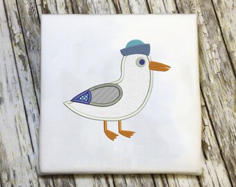 Può includere: Gabbiano ricamato bianco con un cappello da marinaio blu e bianco con un'ala grigia e blu. Il gabbiano è su uno sfondo bianco.