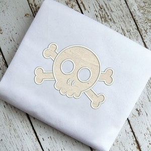 May include: A white fabric with a beige embroidered skull and crossbones design.