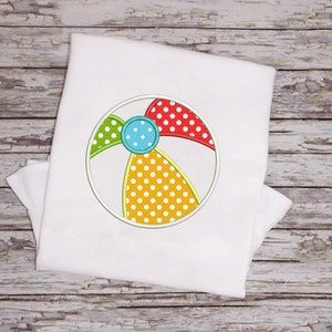 Könnte beinhalten: Ein weißes T-Shirt mit einem bunten gestickten Strandball-Design. Der Strandball ist rot, gelb, grün und blau mit weißen Punkten.