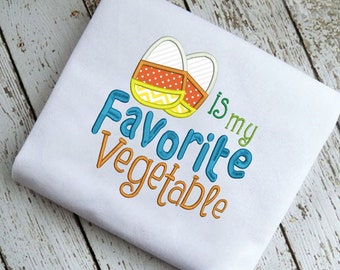 Op de afbeelding: Wit T-shirt met een geborduurd ontwerp van twee oranje en gele snoepmais met de tekst "is my favorite vegetable" in blauw en oranje.