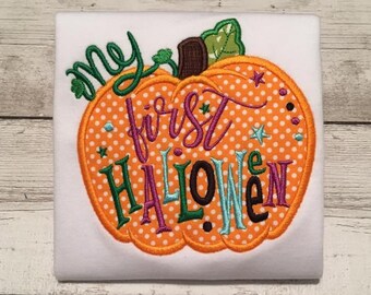 May include: White onesie with an embroidered orange pumpkin with white polka dots. The pumpkin has the text "my first halloween" in colorful letters.