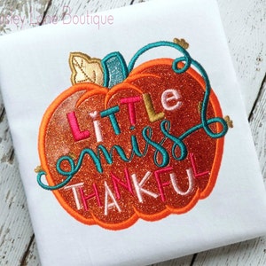 Puede incluir: Calabaza naranja con purpurina con una vid turquesa y las palabras "Little miss thankful" en letras rosa, turquesa y doradas.