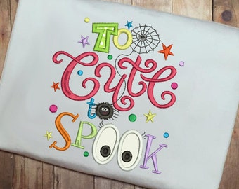 May include: A white fabric with colorful embroidered text that reads "Too cute to spook". The text is surrounded by colorful stars, dots, and a spider with a web.