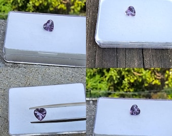 Könnte beinhalten: Vier Bilder zeigen einen herzförmigen, facettierten Amethyst-Edelstein. Der Edelstein hat eine tiefviolette Farbe und wird in einem kleinen, transparenten Kunststoffbehälter mit weißem Innenraum präsentiert. Ein Bild zeigt den Edelstein, der von einer Pinzette gehalten wird.