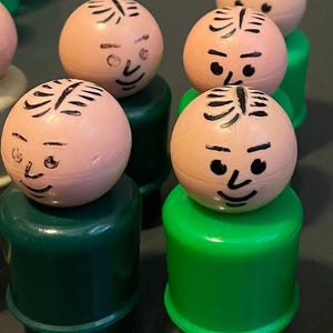 May include: A set of five vintage plastic toy people with green bases and pink heads. Each head has a black painted face with a simple design.