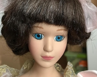 May include: A porcelain doll with brown hair, blue eyes, and a pink dress with gold trim.