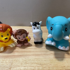 May include: A set of four plastic animal figurines, including a lion with a yellow body and brown mane, a monkey with brown fur, a zebra with black and white stripes, and a blue elephant.