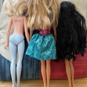 K&ouml;nnte beinhalten: Drei Puppen mit langen Haaren stehen R&uuml;cken an R&uuml;cken. Die Puppe links hat blonde Haare und tr&auml;gt ein hellblaues Kleid. Die Puppe in der Mitte hat blonde Haare und tr&auml;gt ein blaues und rosa Kleid. Die Puppe rechts hat dunkle Haare und tr&auml;gt ein schwarzes Kleid.
