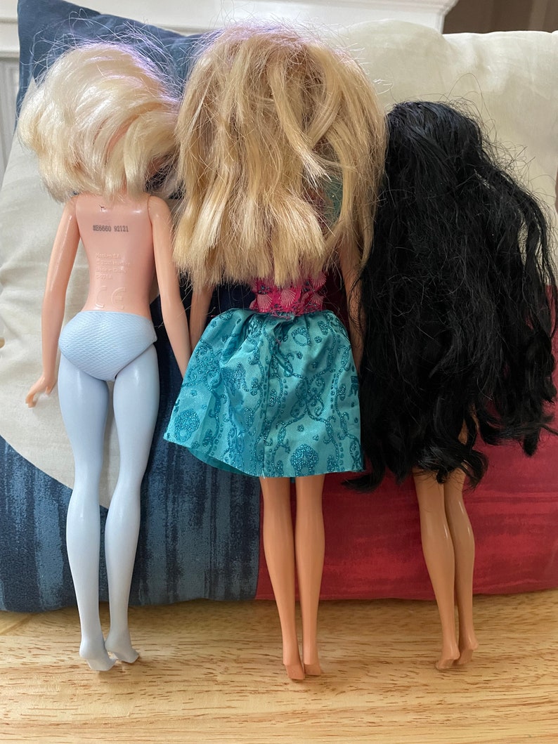 K&ouml;nnte beinhalten: Drei Puppen mit langen Haaren stehen R&uuml;cken an R&uuml;cken. Die Puppe links hat blonde Haare und tr&auml;gt ein hellblaues Kleid. Die Puppe in der Mitte hat blonde Haare und tr&auml;gt ein blaues und rosa Kleid. Die Puppe rechts hat dunkle Haare und tr&auml;gt ein schwarzes Kleid.