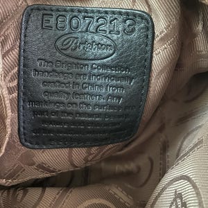 Może przedstawiać: Zbliżenie czarnej sk&oacute;rzanej metki z torebki Brighton. Metka ma numer "E807213" i logo Brighton. Tekst na metce brzmi "The Brighton Collection handbags are individually crafted in China from quality leathers."