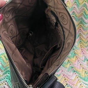 Może przedstawiać: Czarna sk&oacute;rzana torba crossbody ze srebrnym zamkiem błyskawicznym i ciemnobrązową podszewką. Wewnętrzna podszewka ma powtarzający się wz&oacute;r litery "B". Torba ma ciemnoniebieski sk&oacute;rzany pasek.