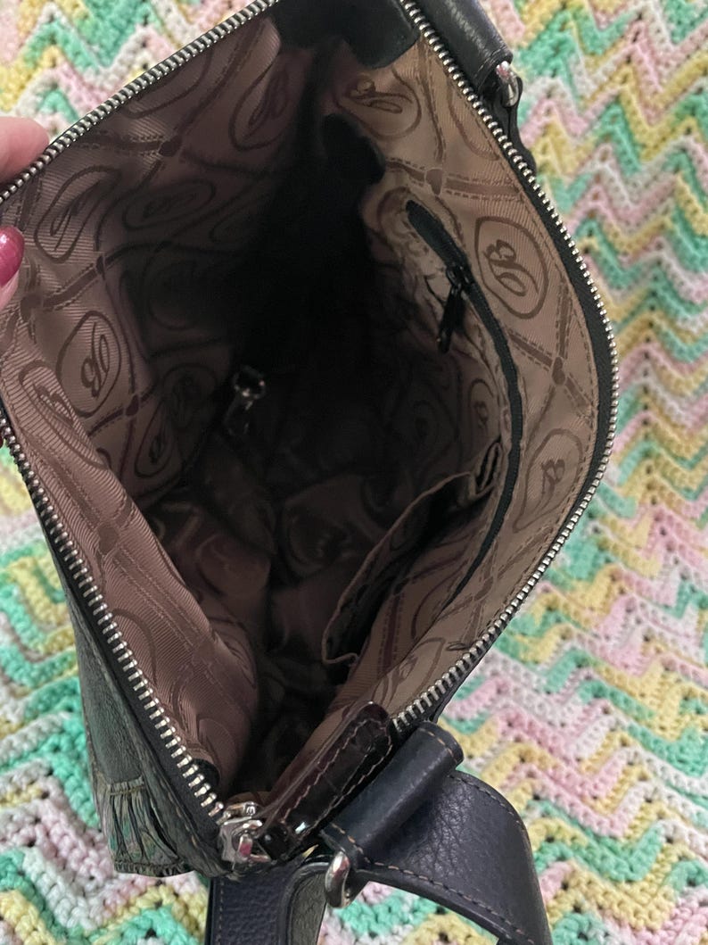 Może przedstawiać: Czarna sk&oacute;rzana torba crossbody ze srebrnym zamkiem błyskawicznym i ciemnobrązową podszewką. Wewnętrzna podszewka ma powtarzający się wz&oacute;r litery "B". Torba ma ciemnoniebieski sk&oacute;rzany pasek.