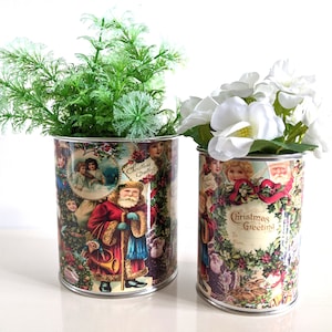 Puede incluir: Dos latas de metal de estilo vintage con diseños navideños. Las latas están decoradas con imágenes de Papá Noel, ángeles y acebo. El texto en las latas dice "Christmas Greetings".