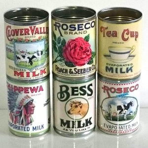 May include: Six vintage metal cans of evaporated milk with different brand names and designs. The cans feature images of a cow, a rose, a teacup, an American Indian, and a cow with the words "Clover Valley", "Roseco", "Tea Cup", "Chippewa", "Bess", and "Roseco" on them.