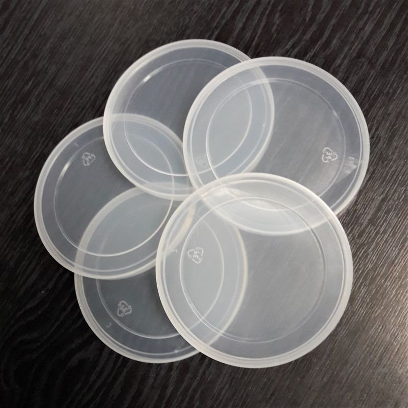 Puede incluir: Cinco tapas de pl&aacute;stico transparente con un s&iacute;mbolo de reciclaje en cada una. Las tapas est&aacute;n apiladas unas sobre otras.