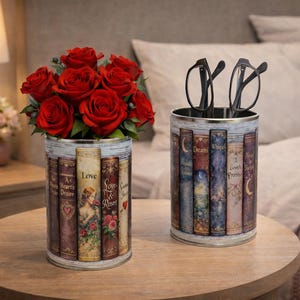 Pode incluir: Duas latas decorativas com design de livro. Uma contém um buquê de rosas vermelhas, a outra óculos. As latas estão em uma mesa de madeira, com uma lâmpada e uma cama ao fundo.
