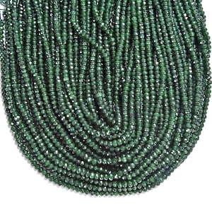May include: A strand of dark green faceted gemstone beads. The beads are small and uniform in size and shape.