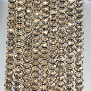 May include: Close-up of strands of faceted, golden-colored pyrite beads. The beads have a metallic sheen and are strung together, creating a textured surface. The beads are oval-shaped with multiple facets, reflecting light. Ideal for jewelry making.
