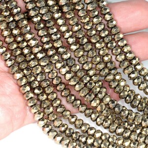 May include: Strands of golden pyrite beads. Each bead is faceted, reflecting light. The beads are strung together, creating a shimmering effect. The beads are a warm, metallic color, and are suitable for jewelry making.