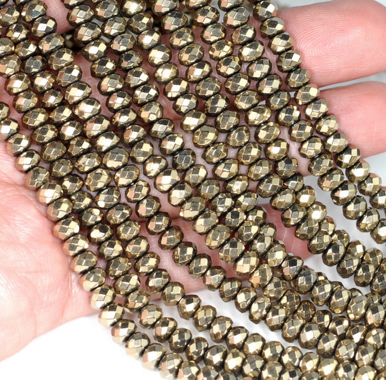 May include: Strands of golden pyrite beads. Each bead is faceted, reflecting light. The beads are strung together, creating a shimmering effect. The beads are a warm, metallic color, and are suitable for jewelry making.