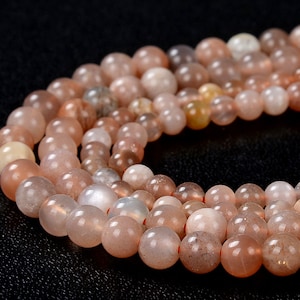 May include: A strand of light pink and white sunstone beads. The beads are round and have a smooth, polished finish.