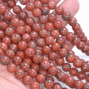 May include: A strand of round, red jasper beads with black and white marbling. The beads are smooth and polished.