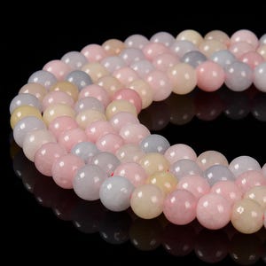 May include: Strands of smooth, round beads in a variety of pastel colors, including pink, gray, and cream. The beads are strung together, creating a curved shape against a black background. The beads appear to be approximately 0.3 inches in diameter.