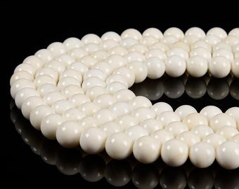May include: A strand of white round beads made from natural bone. The beads are smooth and polished, and they are strung together on a clear thread.