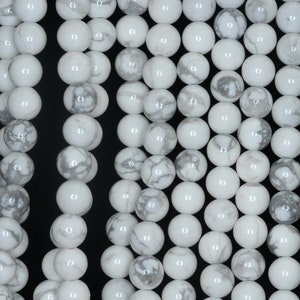 May include: White howlite beads with gray veining. The beads are round and smooth, and they are strung together on a string.