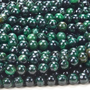 May include: A close-up of a pile of dark green round beads. The beads are made of natural stone and have a smooth, polished finish.