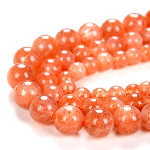 Könnte beinhalten: Eine Kette aus orangefarbenen Sonnenstenperlen. Die Perlen sind rund und haben ein durchscheinendes, funkelndes Aussehen.