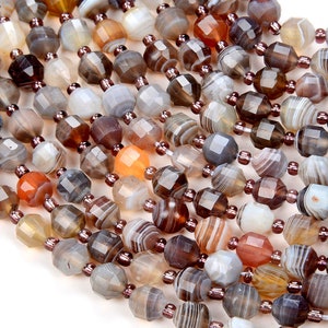 Puede incluir: Una hebra de cuentas de ágata facetadas en tonos marrones, grises y naranjas. Las cuentas son de diferentes tamaños y formas, y tienen un acabado natural y pulido.