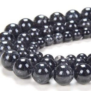 May include: A strand of black gemstone beads with a silver-grey shimmer. The beads are round and smooth, and they are strung on a clear thread.